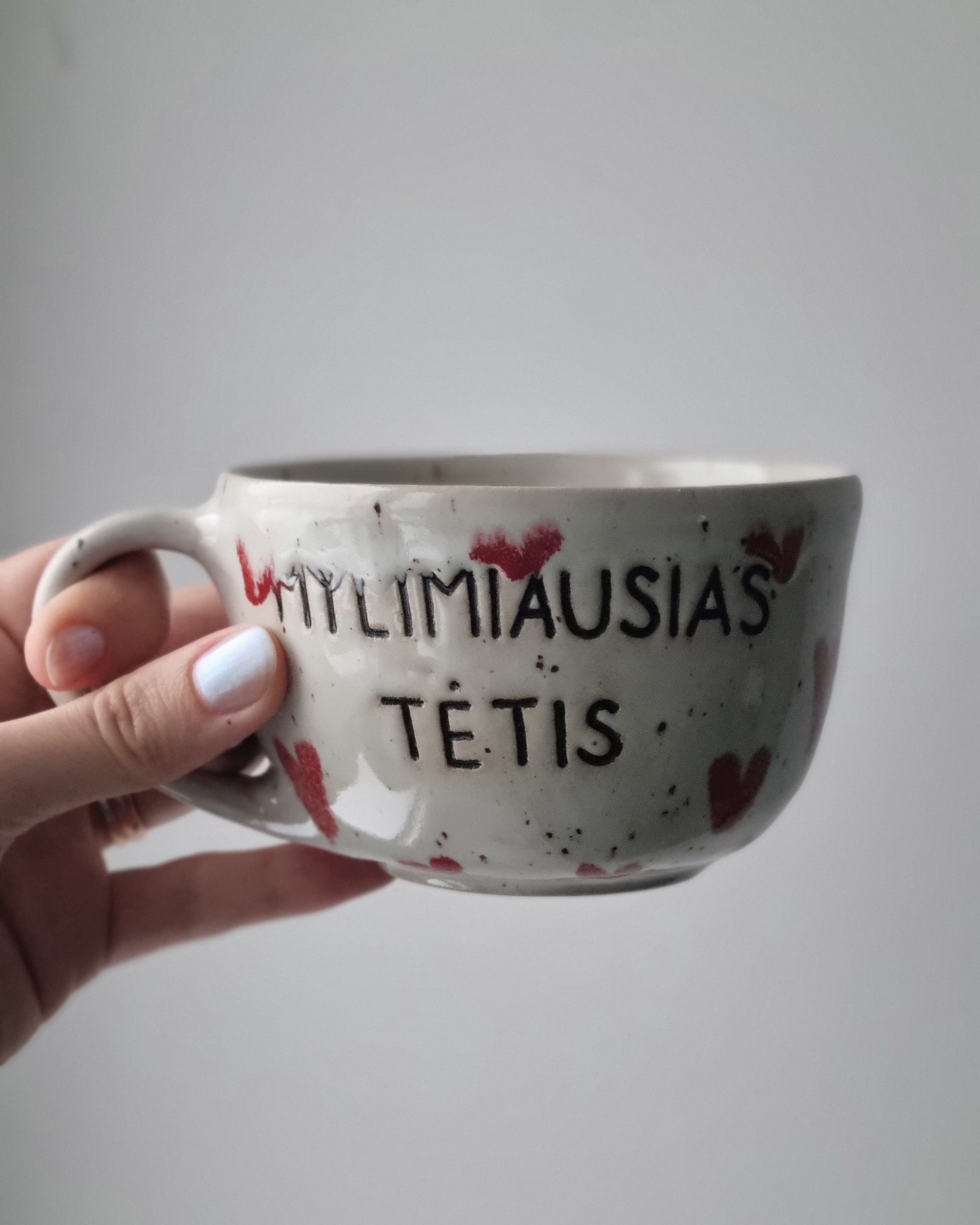 Hand holding a mug with text and heart designs against a plain background