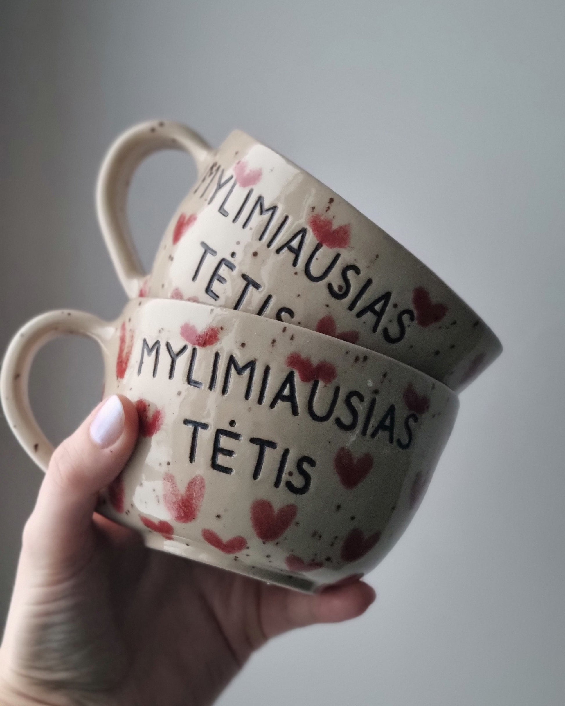 Two ceramic bowls with decorative text and heart patterns held by a hand against a plain background.